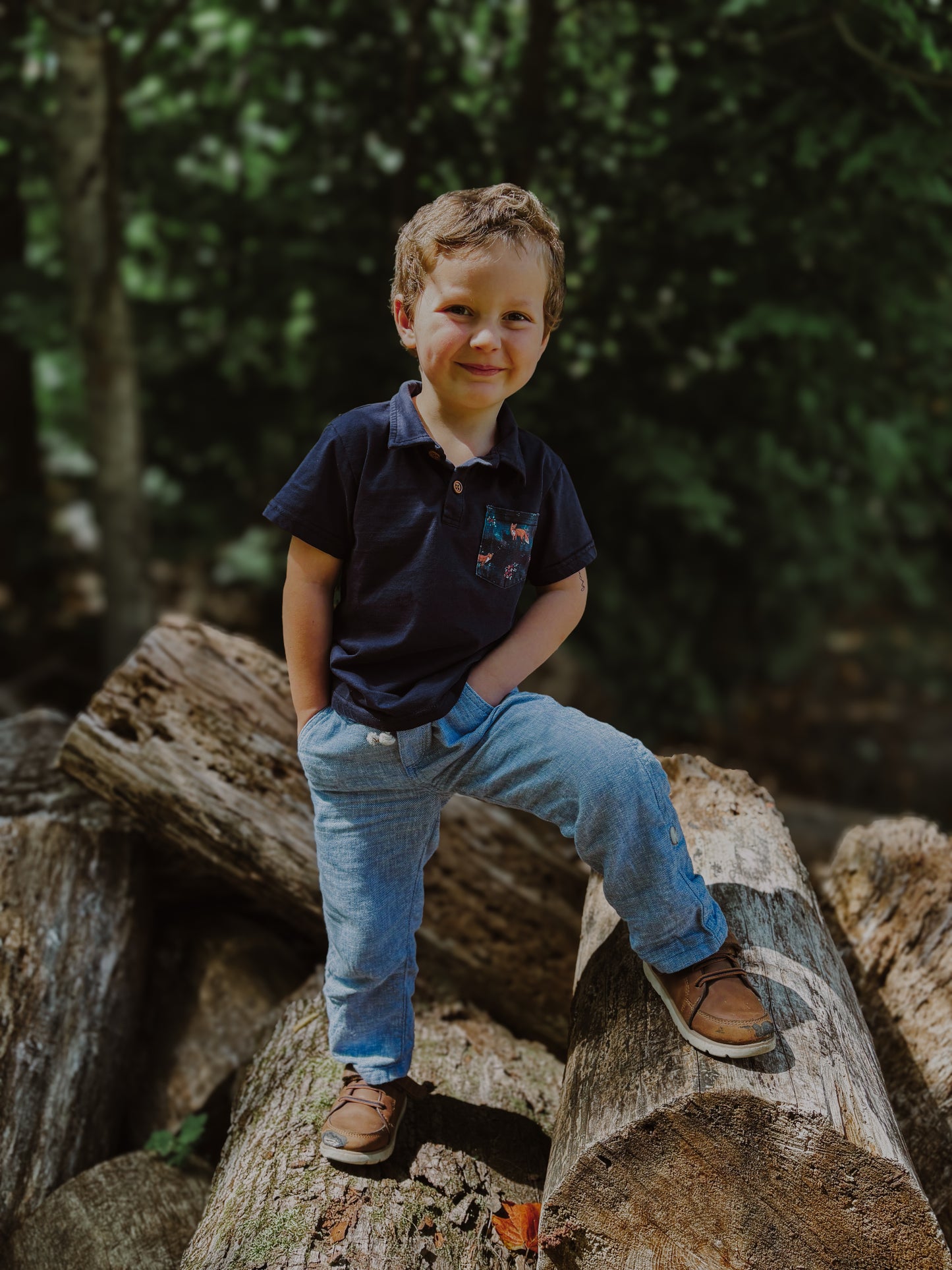 Boy sitting on log in forest.