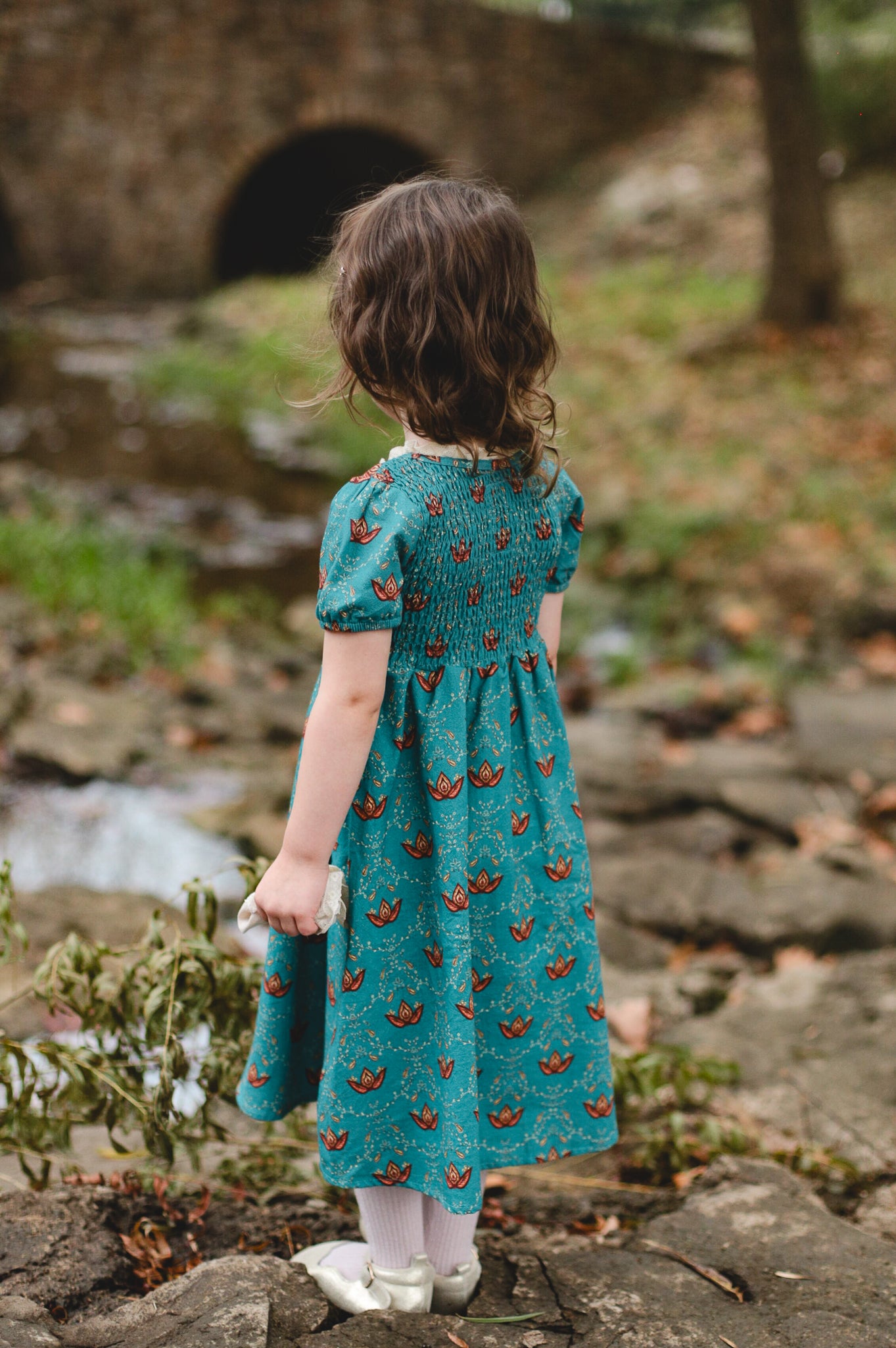 Young girl wearing modest dress near stone bridge