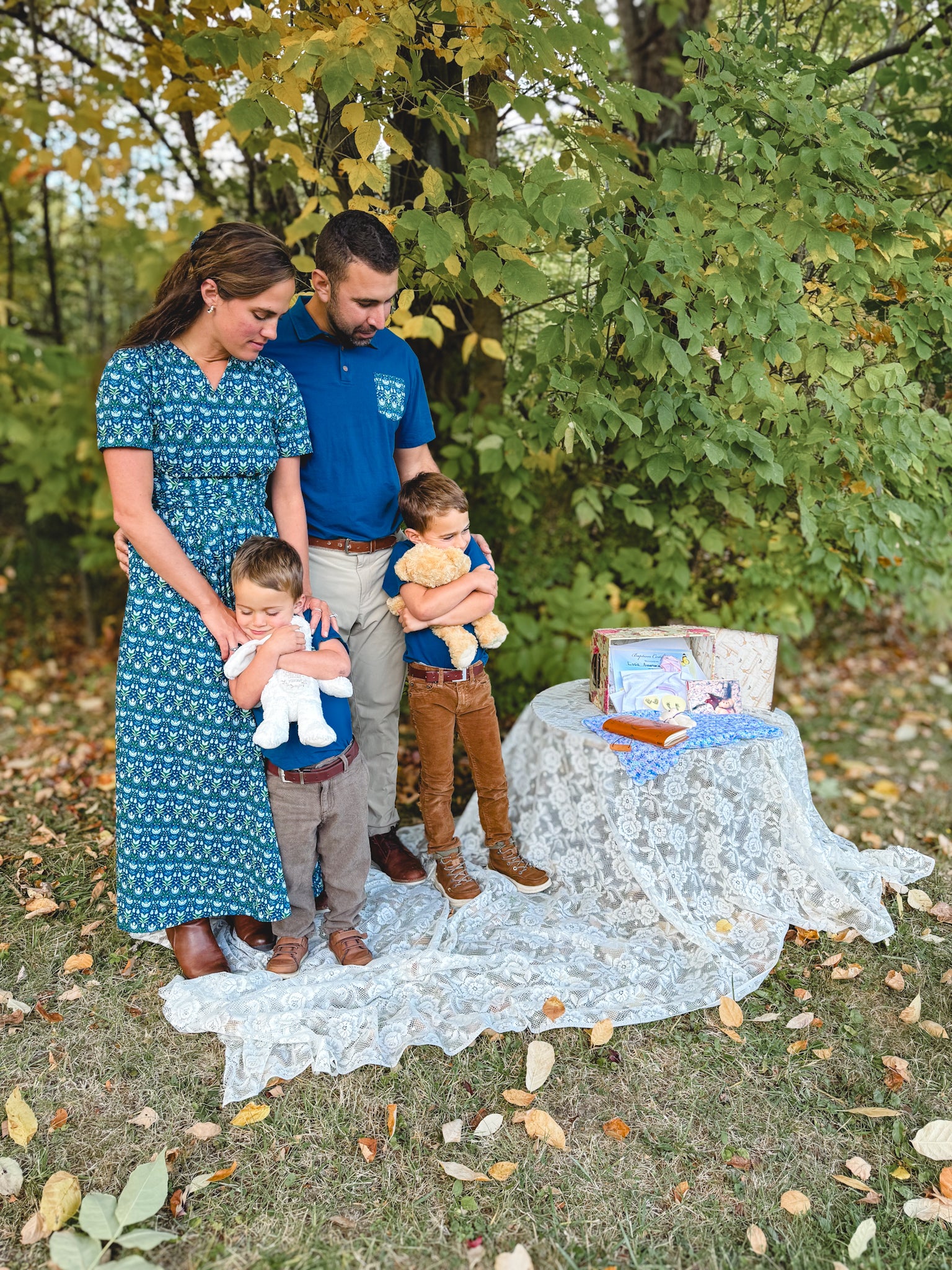 Family of four outdoors with baby shower gifts and setup.