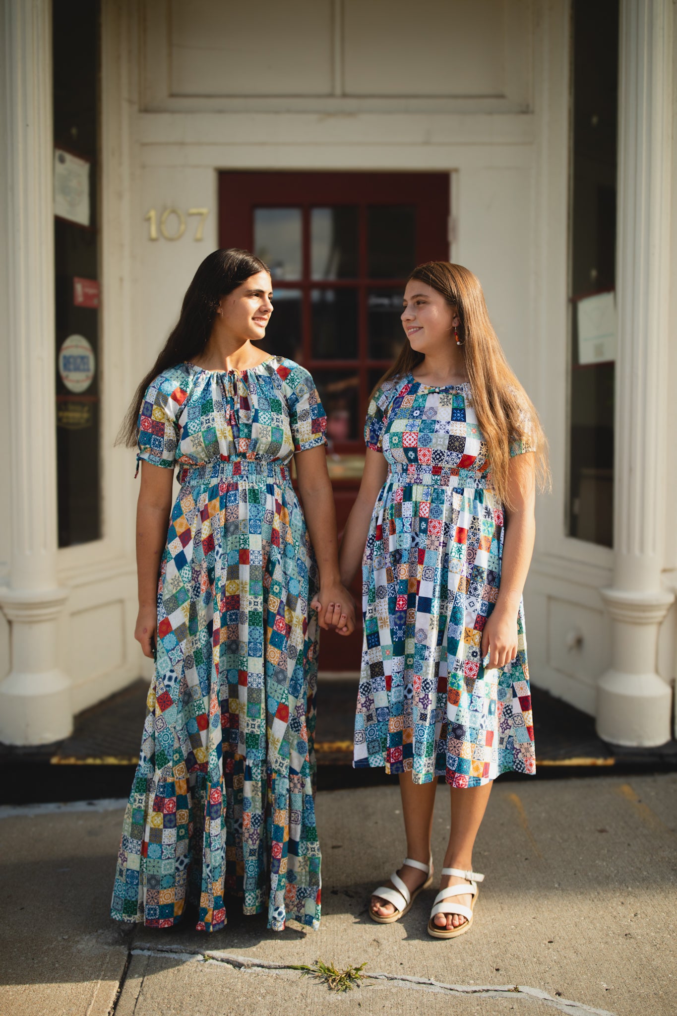 Two women wearing colorful patterned modest dresses standing outside a building.