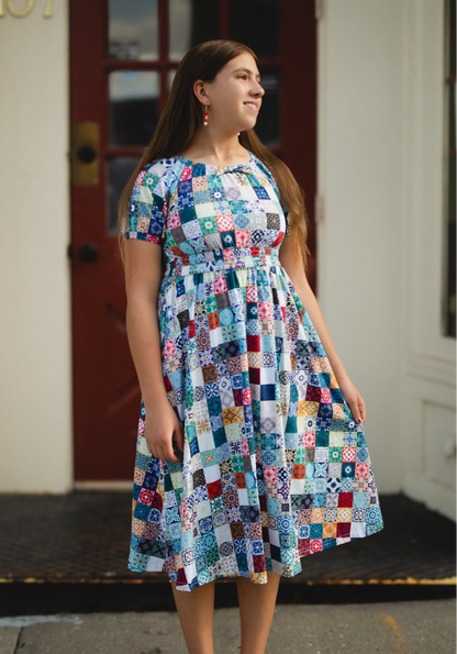 Woman wearing a colorful patchwork modest nursing dress standing in front of a building entrance.