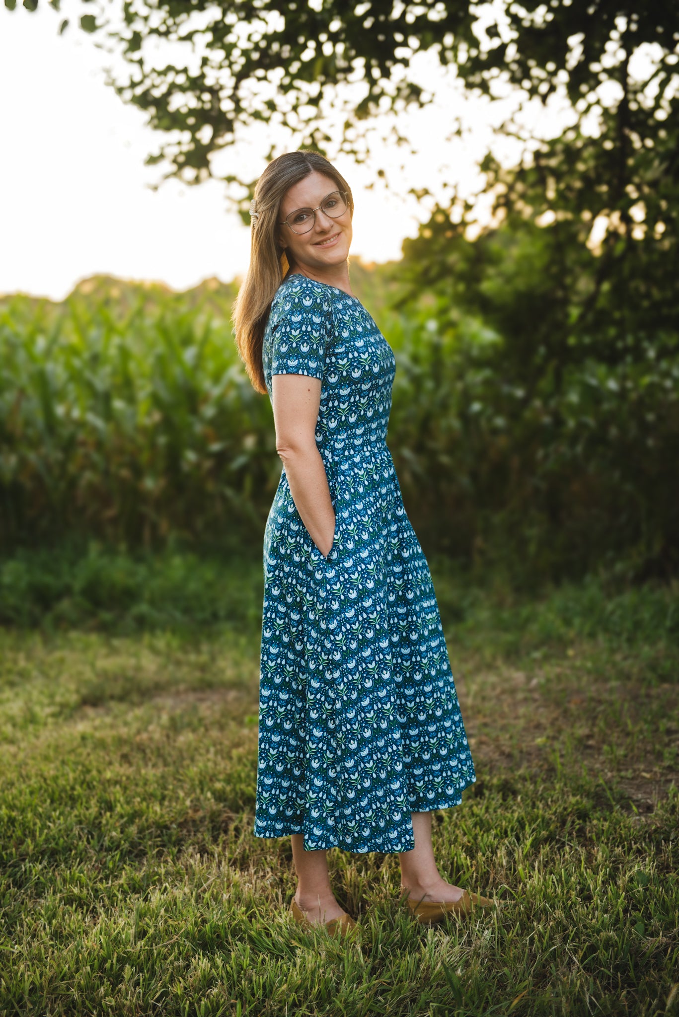 Woman in modest nursing dress, grassy field trees.