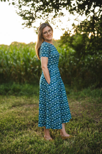 Woman in modest nursing dress, grassy field trees.