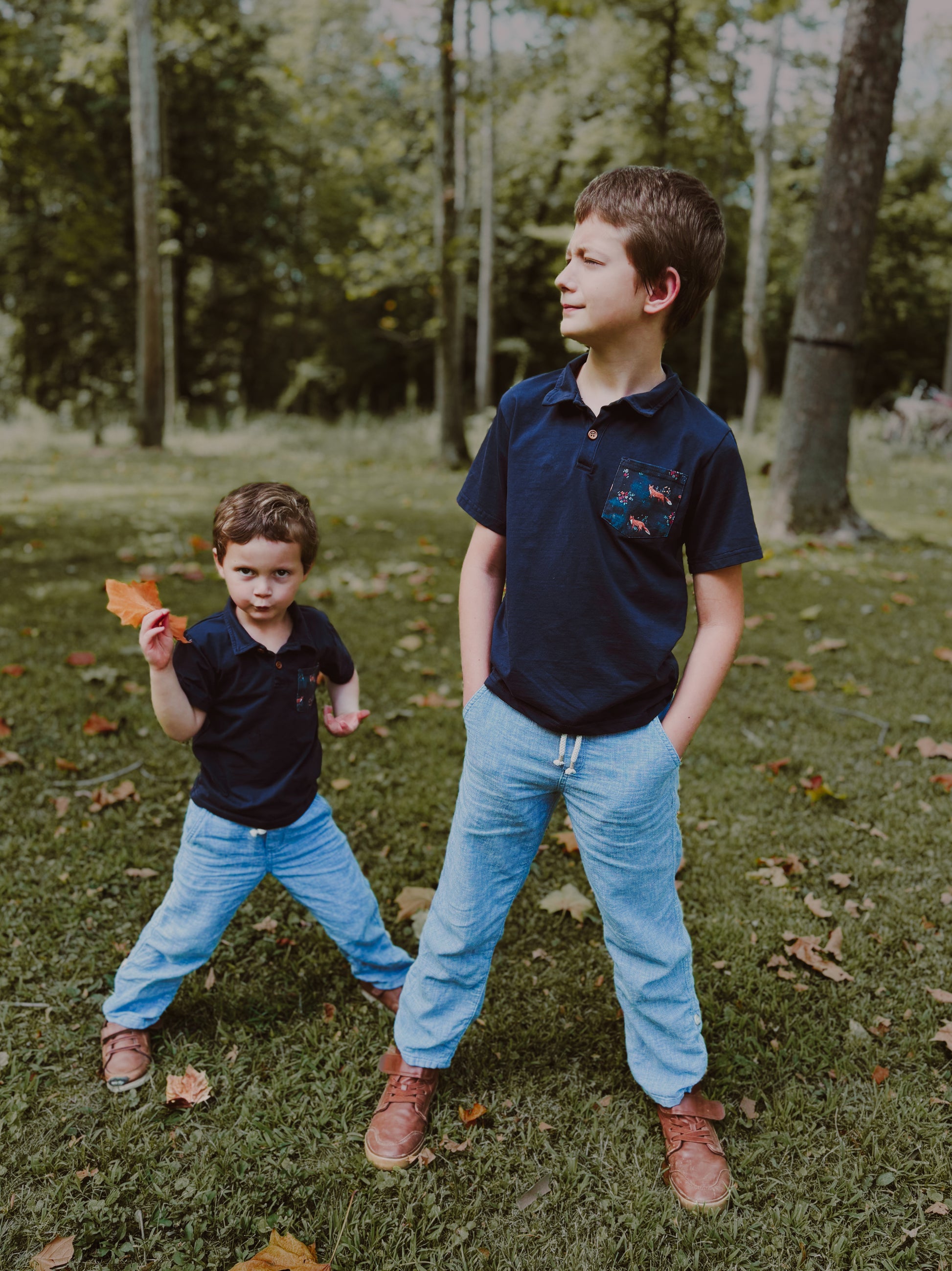 Two boys standing in grass with trees.