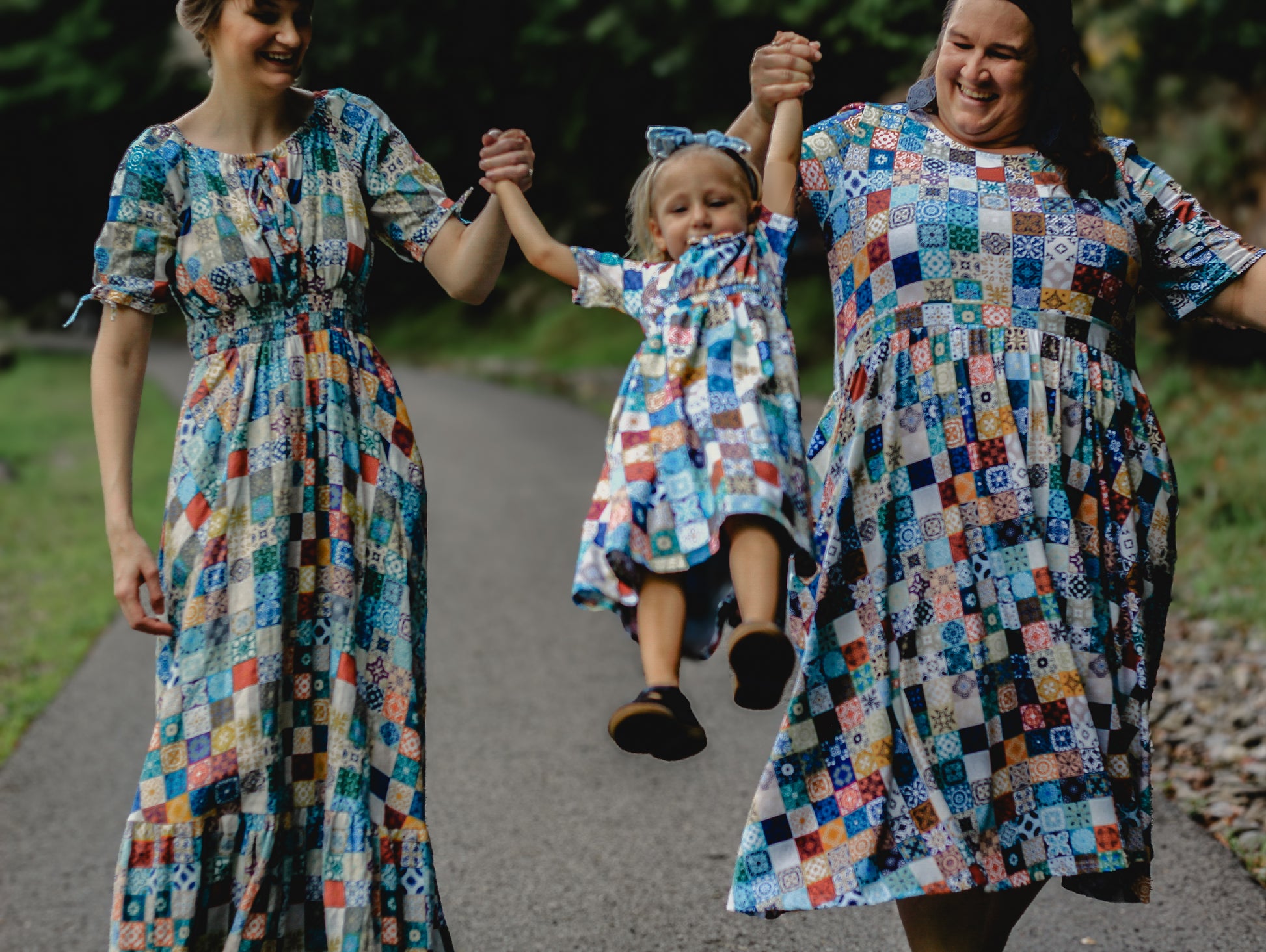 Three women in colorful patterned modest dresses holding hands outdoors.