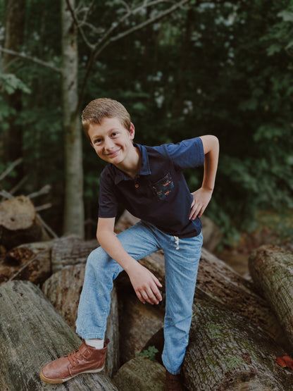 Boy sitting on logs in forest.