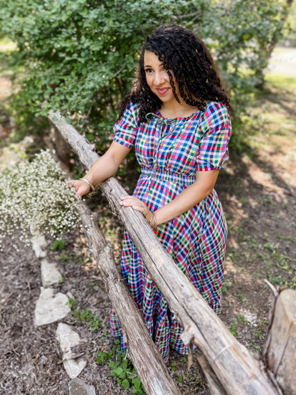 Woman in a colorful modest nursing dress standing outdoors near a wooden fence with greenery in the background
