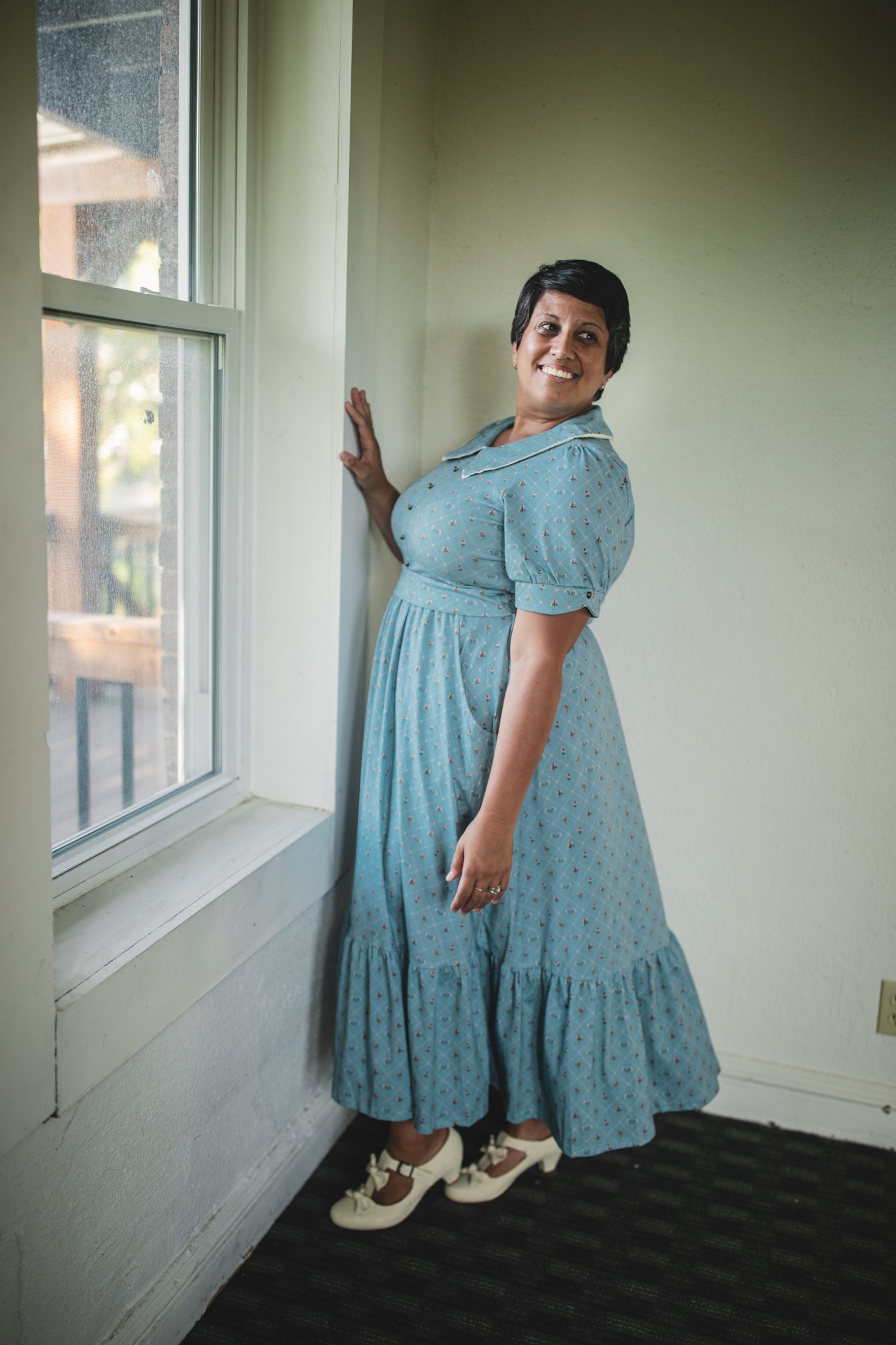 Woman in a blue modest nursing dress standing by a window indoors