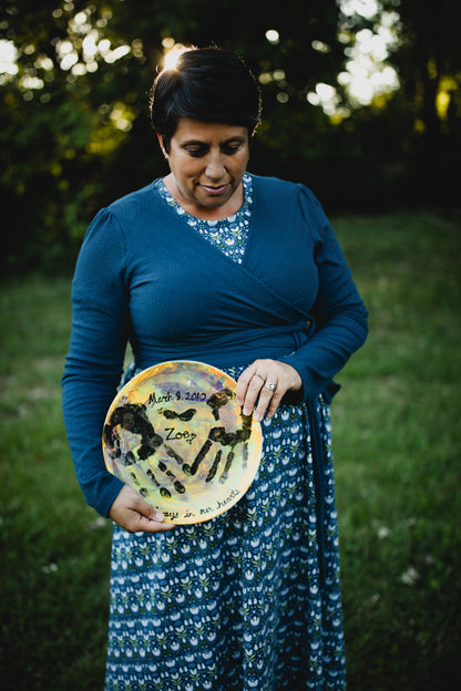 Woman in modest nursing dress with handprint plate outdoors.